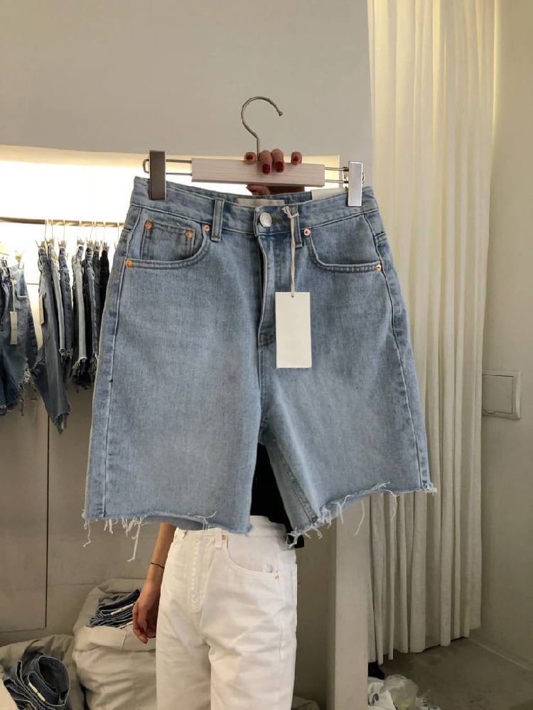 Shorts Jeans Feminino Casual Solto de Cinco Pontos exibidos em um cabide com etiqueta, estilo verão e design moderno.